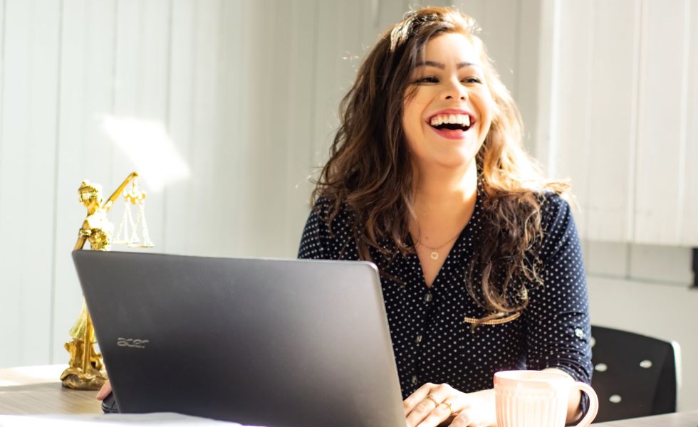 A person is sitting at a desk in front of a laptop, and they're looking to their right and laughing.
