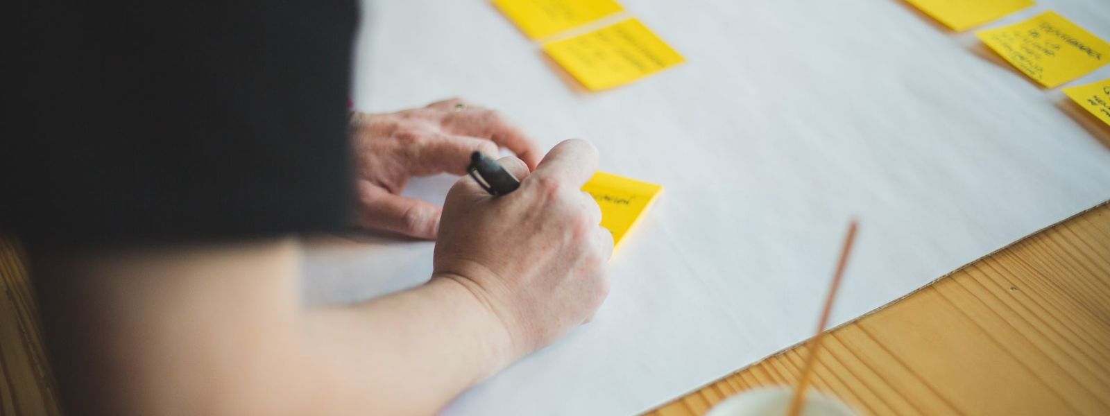 Someone is writing on yellow post-it notes and sticking them on a large piece of paper in 2 horizontal lines.