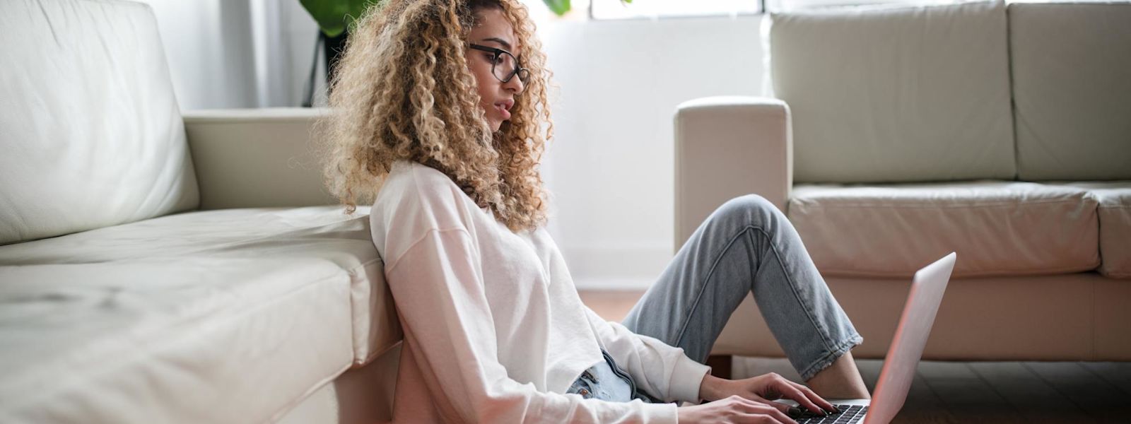 A woman sits on the floor in her lounge on her laptop.