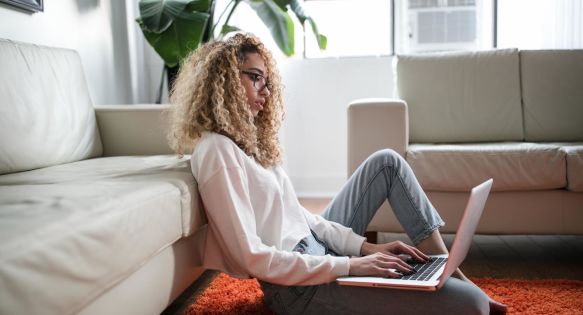 A woman sits on the floor in her lounge on her laptop.