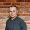 Rory Breach, Account Executive at Karbon. Rory is standing in front of a red brick wall, has a buzzcut and is wearing a dark gray collared shirt.