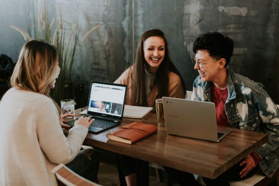 3 people sitting around a cafe table with their laptops, working and laughing.