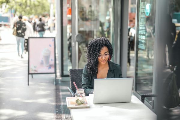 Someone is sitting at an outdoor cafe table, typing on a laptop.