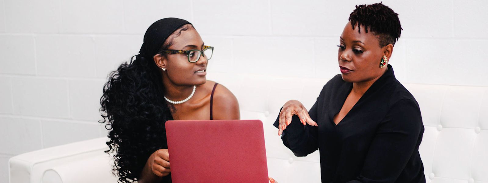 Two women sitting on a couch look at a laptop screen together.