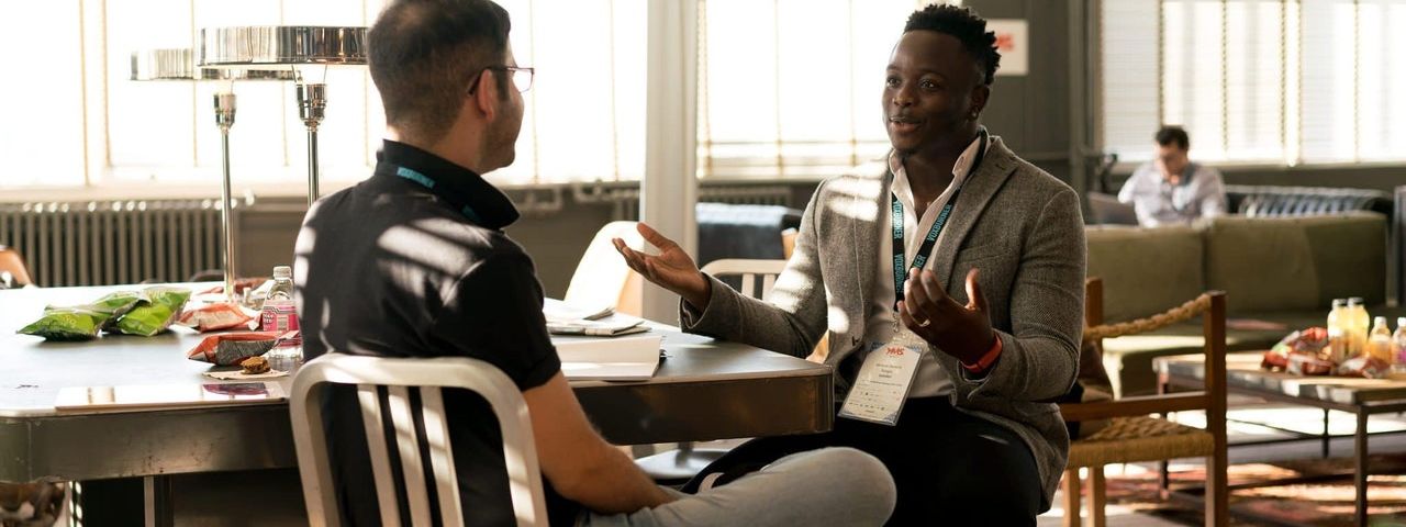 Two people sitting opposite each other at a table, in conversation.