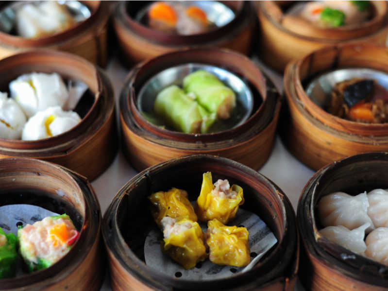 Table full of colourful traditional dim sum dishes in bamboo steamers 