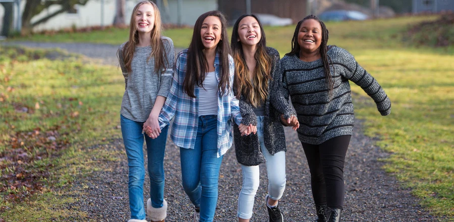 Cuatro chicas sonrientes caminando por un camino de grava