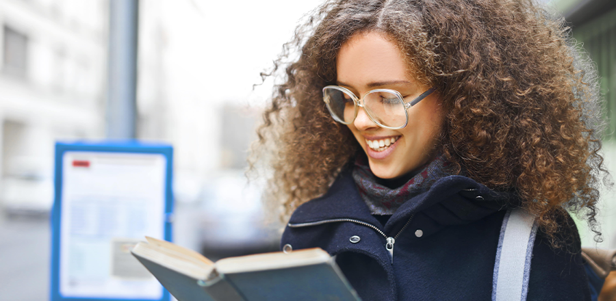 Una mujer sonriente de pie en una parada de autobús leyendo un libro