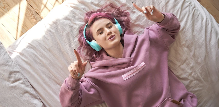 Una mujer tumbada en la cama escuchando música con auriculares