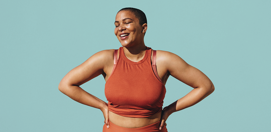 Una joven en ropa deportiva se apoya en una pared con las manos y hace ejercicios flexionando una pierna. 