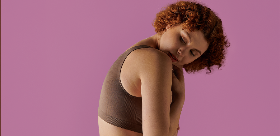 En un banco entre la vegetación una joven sentada con sombrero y auriculares en el cuello. Levanta la vista y sonríe.