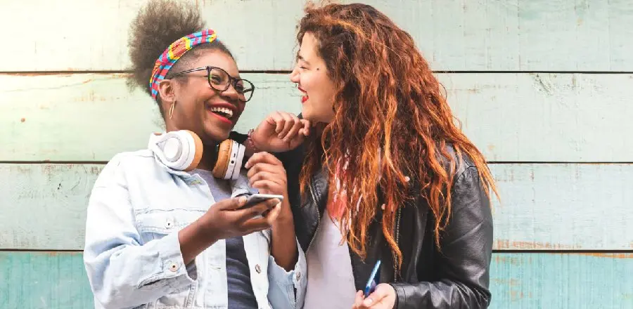 Dos chicas sonriendo y mirándose frente a una pared