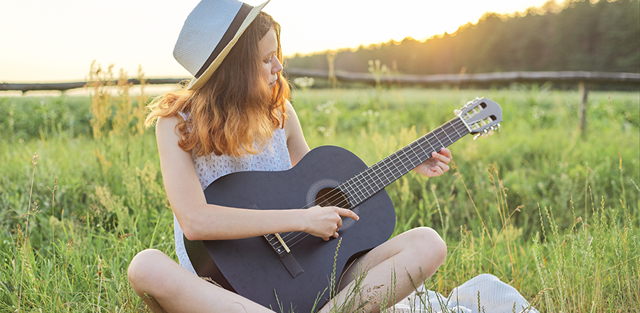 Una mujer sentada en el césped, tocando la guitarra