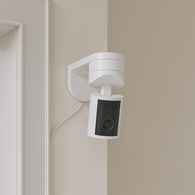 Cámara White Pan-Tilt Indoor Camera 2K montada en pared cerca de puerta con cable de alimentación visible.