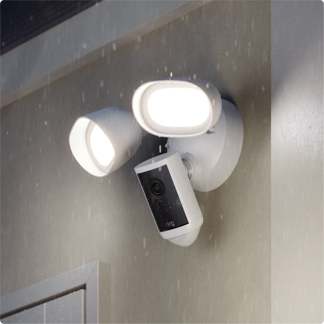 Witte Floodlight Cam Pro (2de generatie) die 's nachts aan de zijkant van een woning is gemonteerd, waarbij beide schijnwerpers branden.
