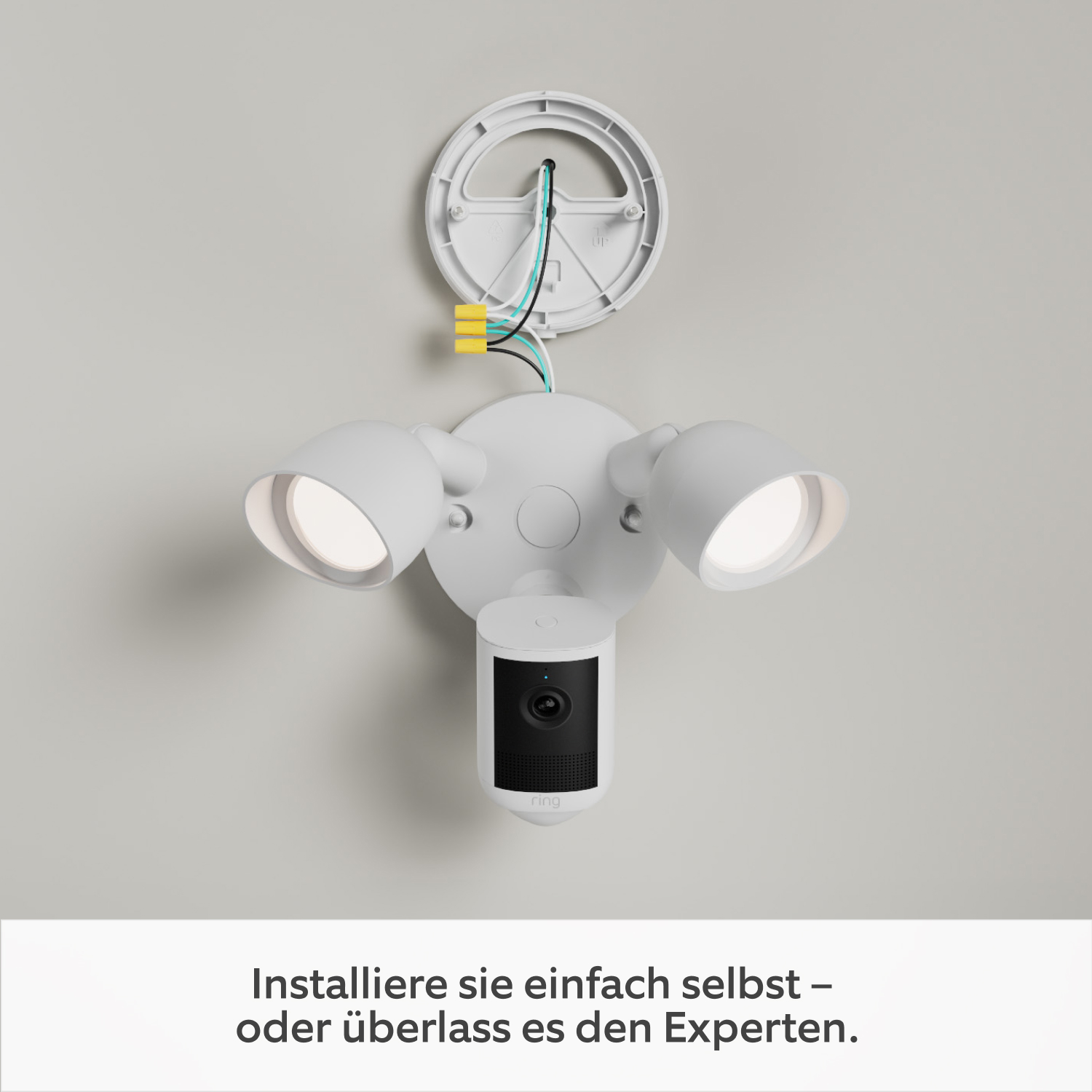 2-Pack Floodlight Camera 2K - Floodlight Cam (2. Gen.) an einer weißen Wand. Die Montageplatte ist an der Wand befestigt und über Kabel mit dem Hauptteil des Geräts verbunden, das unten hängt.