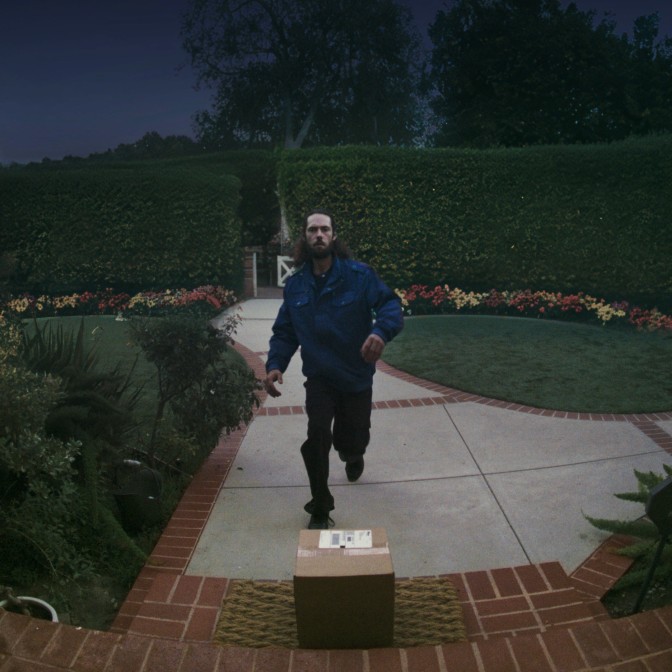 A person walking up a dimly lit pathway toward a package placed on a doorstep.