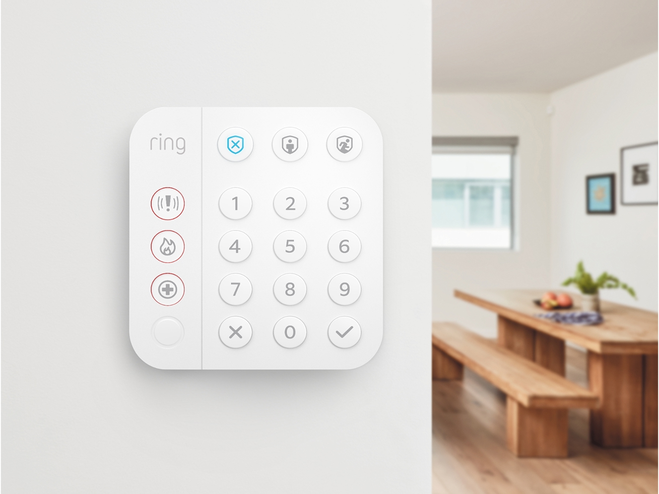 Wall-mounted Ring Alarm Keypad with emergency buttons, installed in a modern home interior near a dining area.