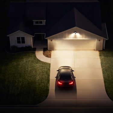 Vue aérienne de nuit d'une allée résidentielle illuminée par la Floodlight Cam (2e gén.) avec une voiture garée devant le garage.