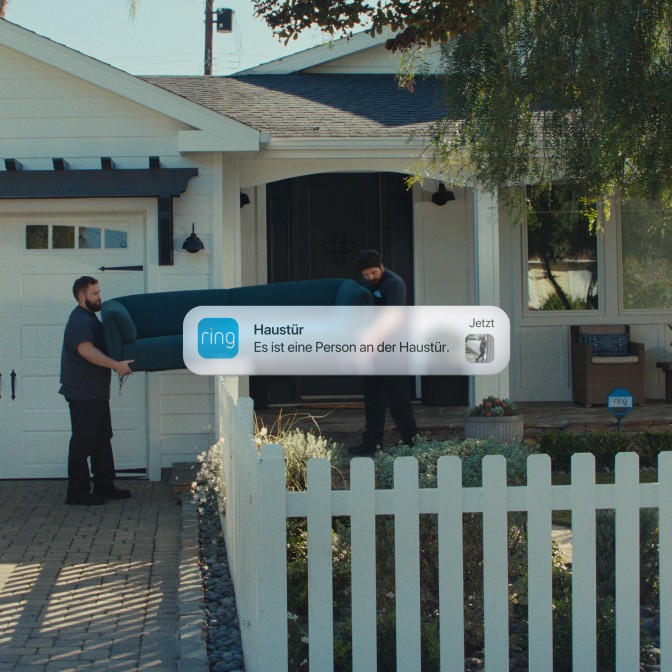 Vorderansicht eines Hauses mit einem von zwei Umzugshelfern im Bild, der eine Couch trägt