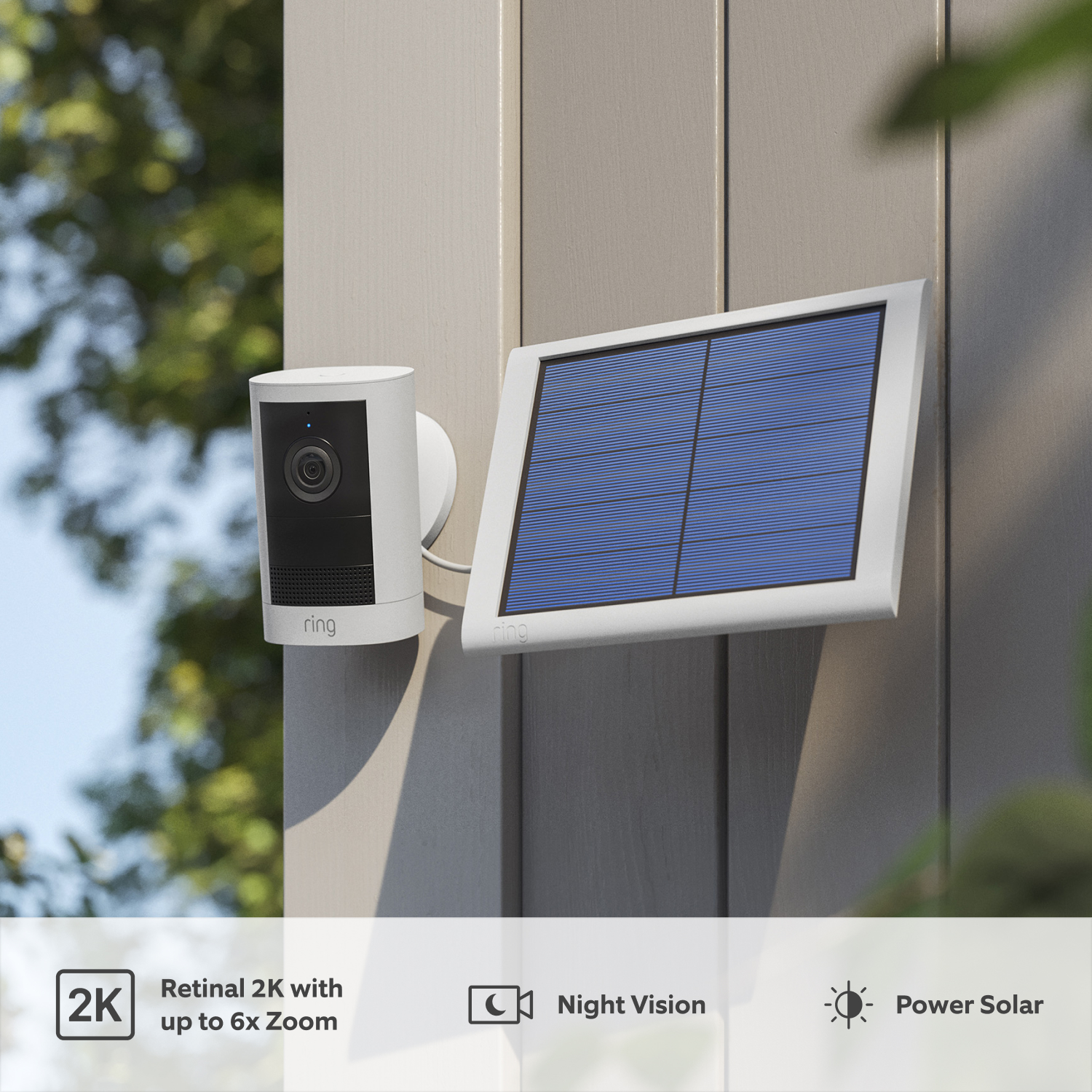 Outdoor Camera Solar (newest generation) - White Ring Outdoor Camera (2nd Gen) mounted on a grey exterior wall, with black lens and solar panel. Foliage in background.