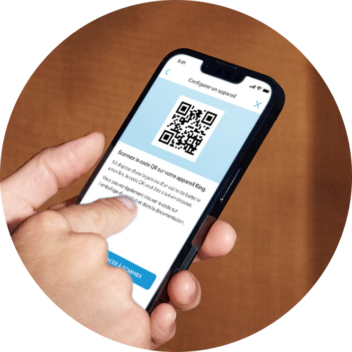 Main tenant un téléphone montrant l'écran de configuration de l'app Ring avec code QR pour la connexion.