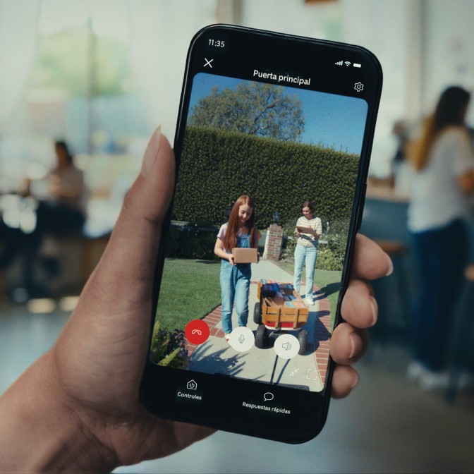 Primer plano de alguien sosteniendo un smartphone que muestra imágenes de una niña y una mujer en un camino, entregando paquetes.