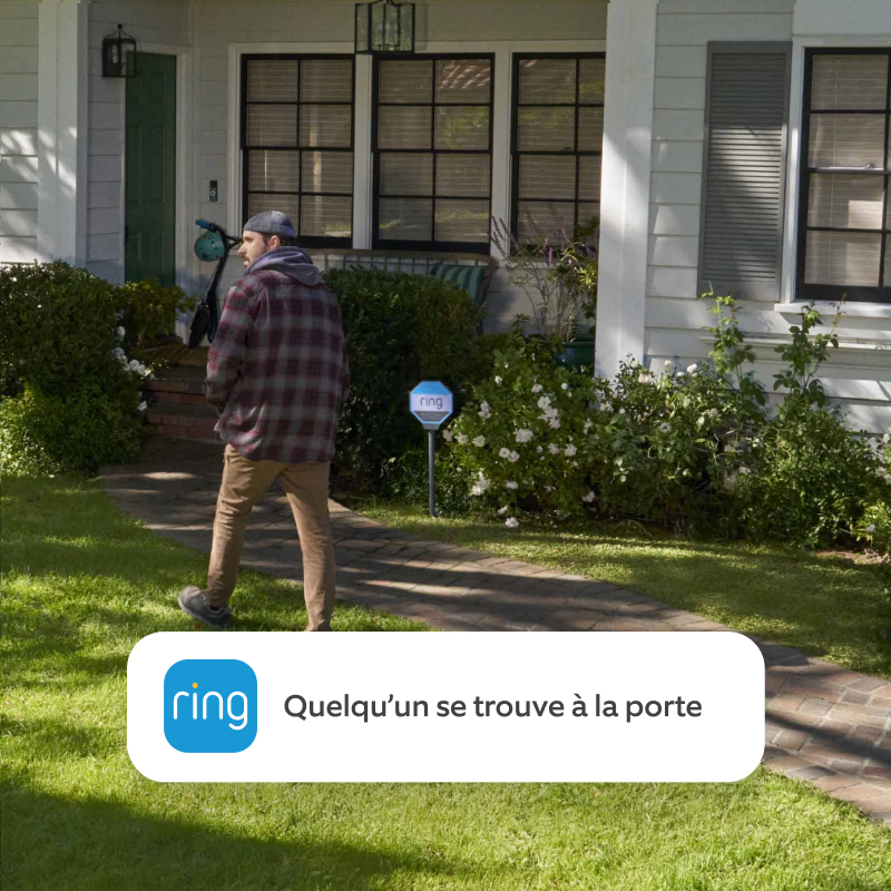 Un homme marche dans l’allée menant à la porte d’entrée d’une maison. Le texte du visuel indique « Quelqu’un s’approche de votre porte d’entrée ».