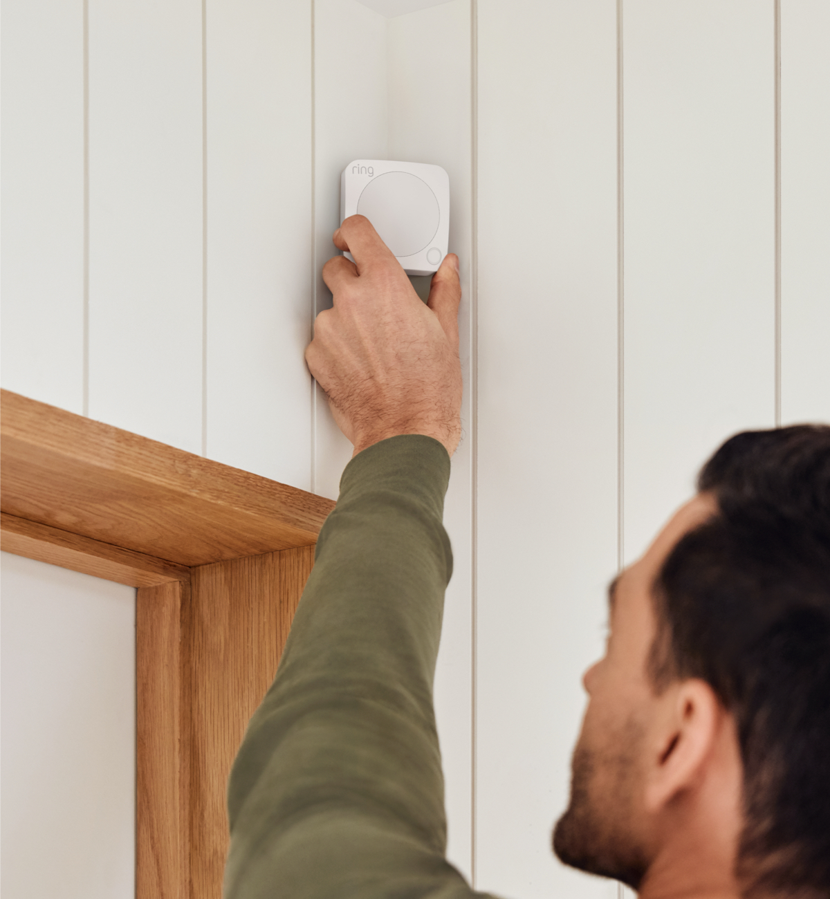 Man installs a Ring Motion Detector above a doorway, illustrating simple DYI setup for Ring Alarm home security system.
