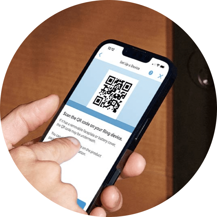 Hand holding phone displaying Ring app setup screen with QR code for device connection and configuration.