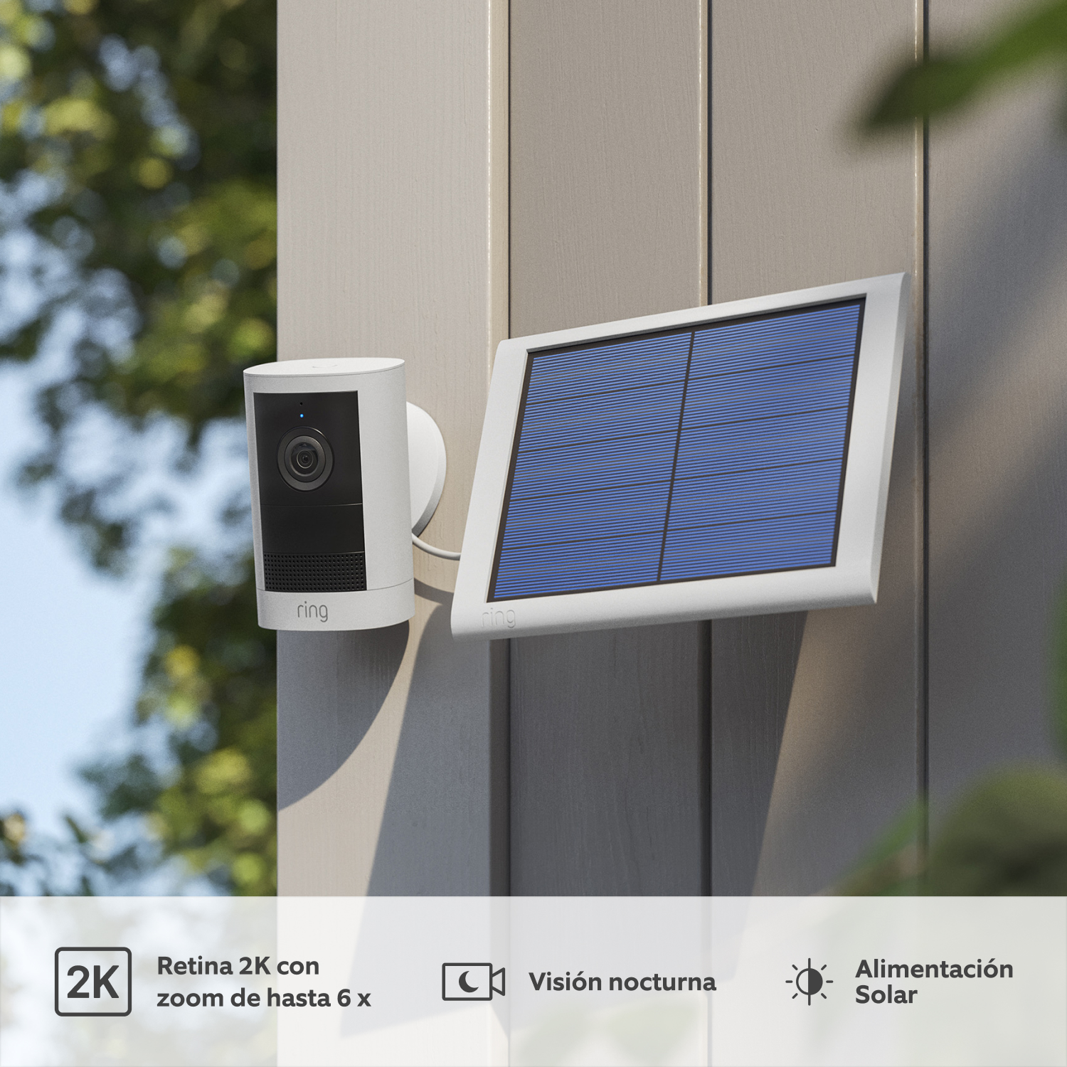 Outdoor Camera 2K Solar - Ring Outdoor Camera (2nd Gen) blanca en pared gris exterior, con lente negra y panel solar. Follaje al fondo.