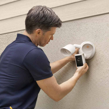 Un homme en polo bleu marine installant la Floodlight Cam (2e gén.) sur un mur extérieur.
