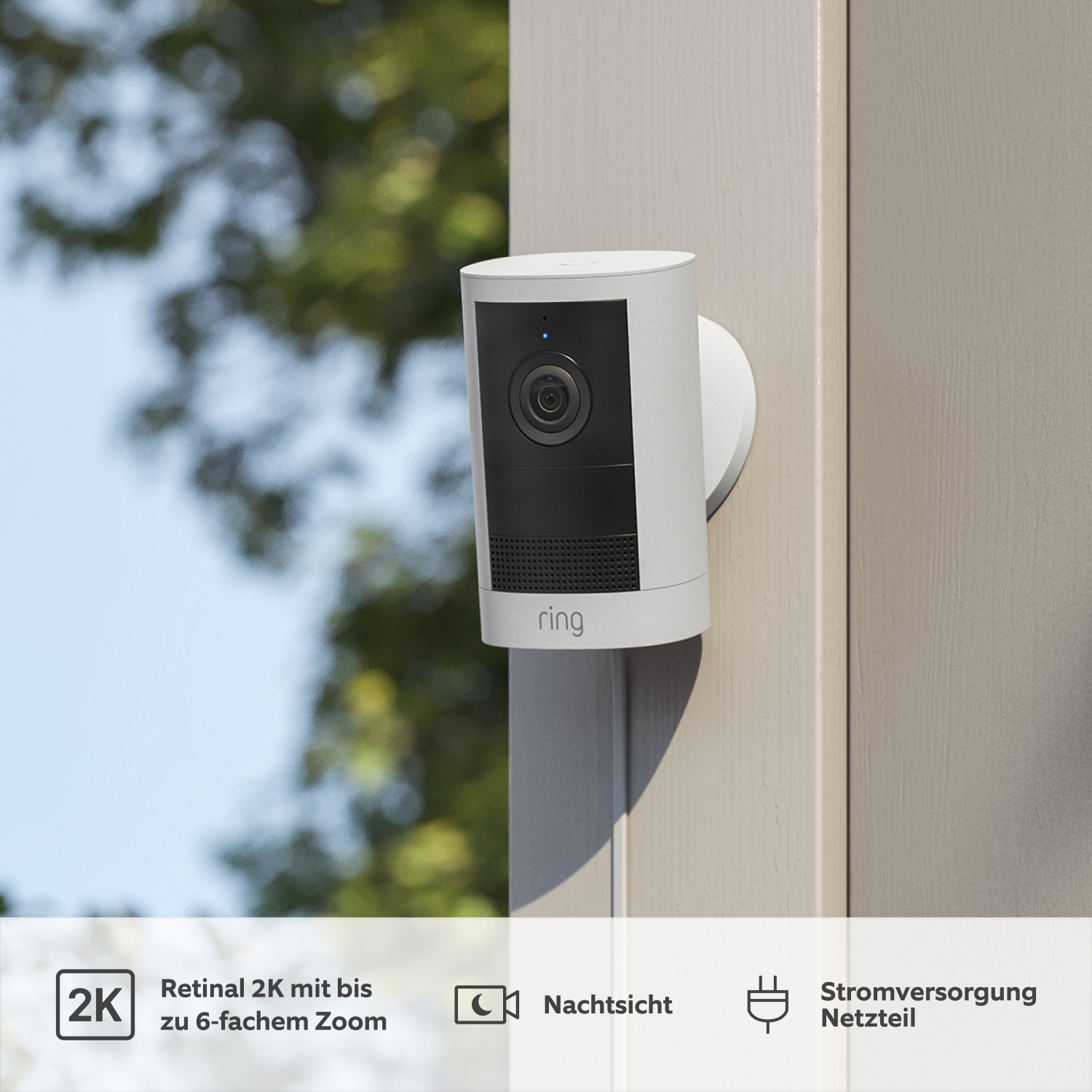 Außenkamera mit Netzteil (neueste Generation) (for Outdoor Camera Plug-in) - White Ring Outdoor Camera (2nd Gen) an grauer Außenwand montiert, schwarze Linse und Lautsprechergitter. Laub im Hintergrund.
