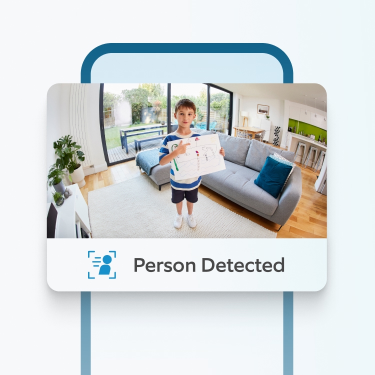 Ring Indoor Camera detects child in lounge holding a drawing as Ring app displays real-time Person Detected alert.