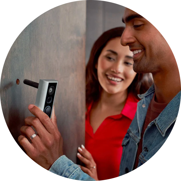 Coppia sorridente installa Ring video doorbell sulla porta dell'appartamento, mostrando la facilità di montaggio.