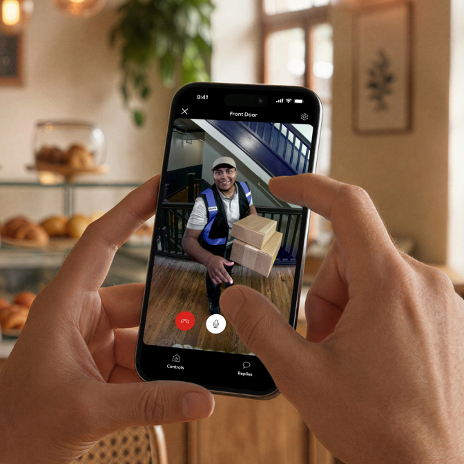 At a restaurant, a person uses their phone to watch a live Peephole Camera 2K feed of a courier delivering a package to their door.