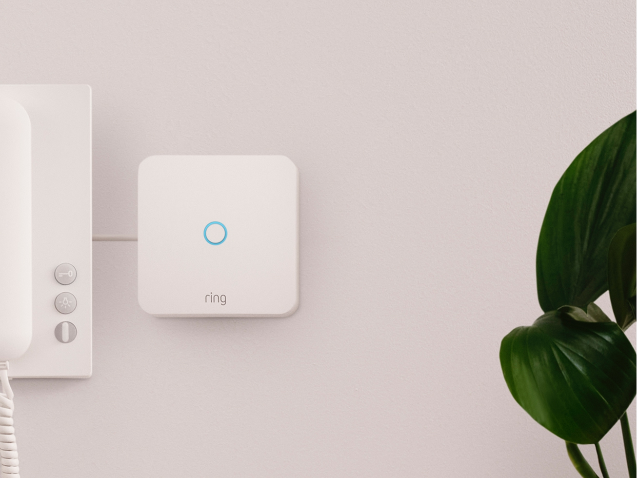 Appareil Ring Intercom fixé au mur à côté d'un combiné téléphonique traditionnel, avec plante verte au premier plan.