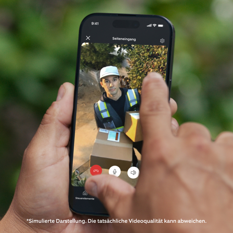 Hand hält Smartphone mit Ring App Live-Feed einer Outdoor Camera (2nd Gen), Vogelperspektive auf Person im blauen Hemd.
