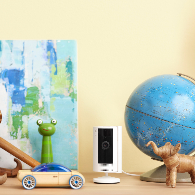 Ring Indoor Camera sits on a chest of drawers with a globe, wooden animals and model car. 