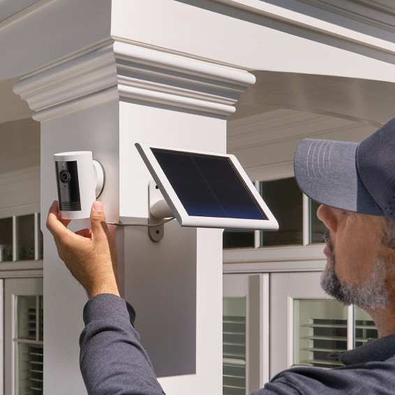 Man installs Ring Outdoor Camera Plus on pillar near solar panel, showing powered outdoor setup.