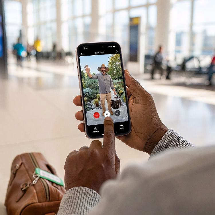 Close-up of someone holding a smartphone displaying footage of a gardner with a hat in front of the door