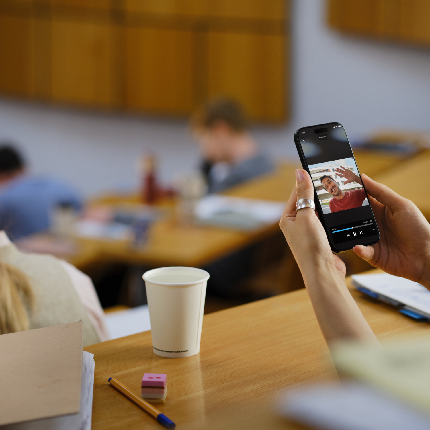 Afbeelding van een vrouw in een auditorium met een smartphone waarop het Ring App-scherm te zien is.