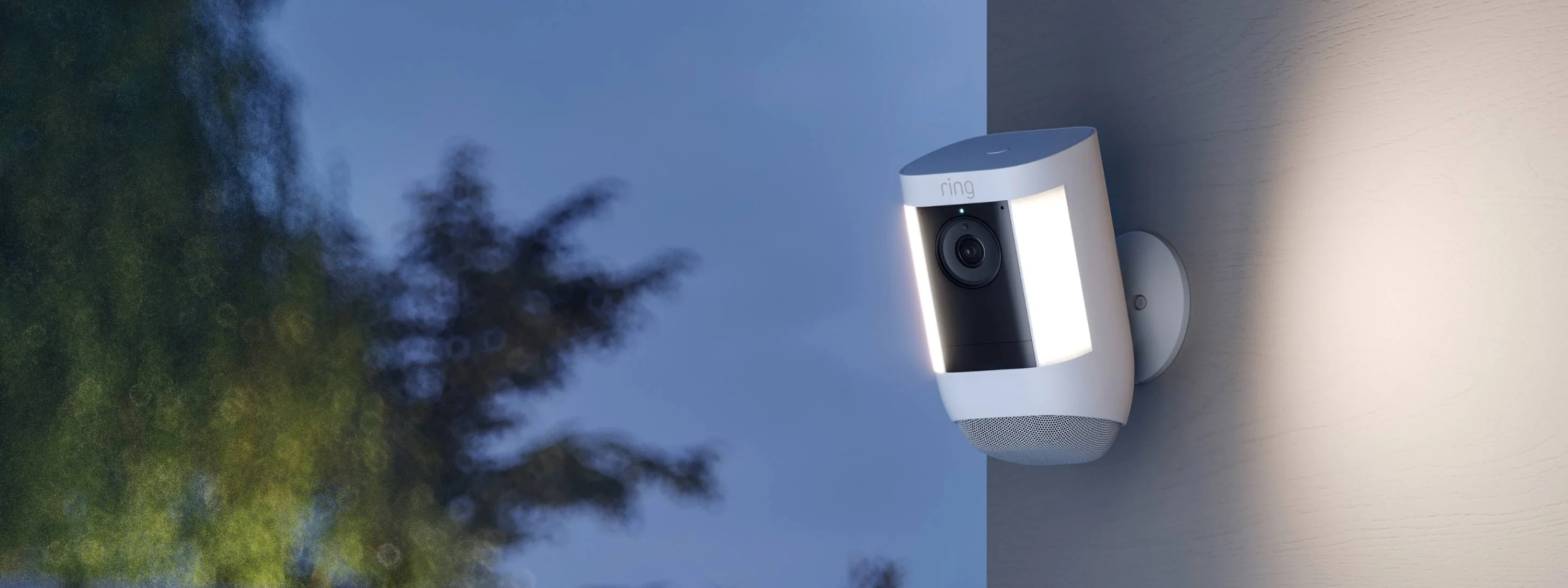 Ring Spotlight Cam Pro montata su parete esterna al crepuscolo con luci laterali accese per visibilità notturna.