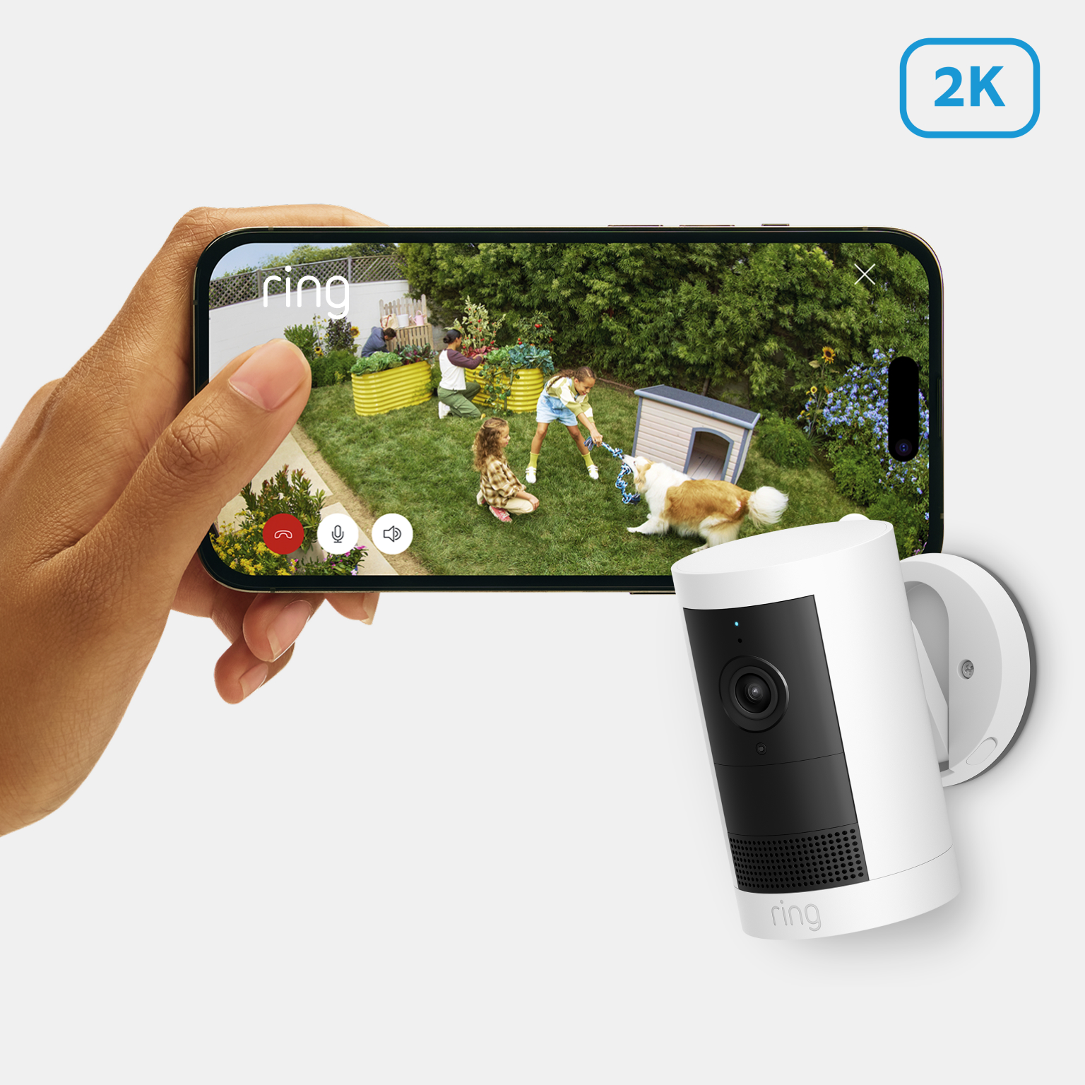 Smartphone shows Ring 2K camera footage of children and dog playing in garden, next to wall-mounted camera.