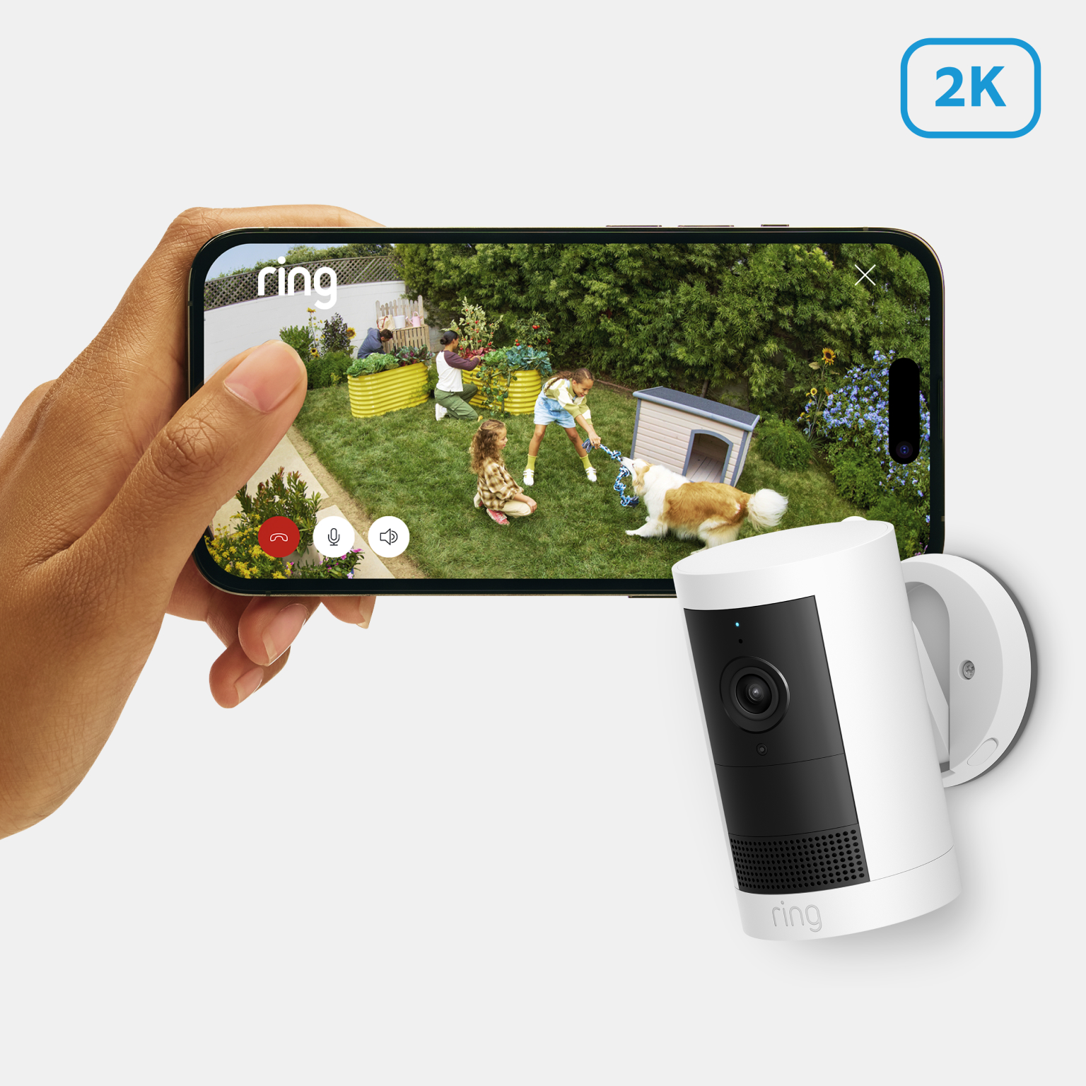 Person holding phone showing Ring 2K camera footage of children and dog playing in garden, next to wall-mounted camera.