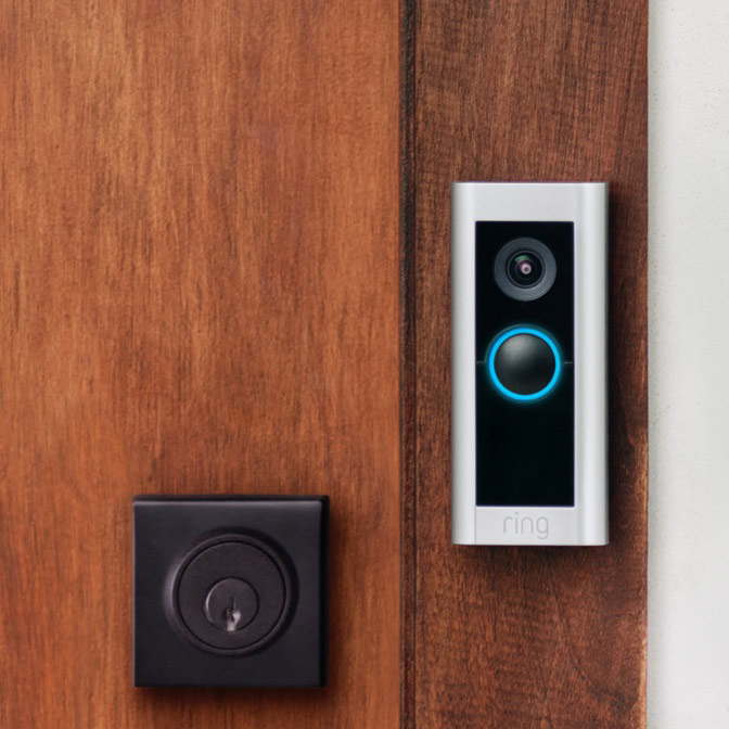 Ring Video Doorbell Pro 2 with glowing blue button mounted beside lock on wooden front door.
