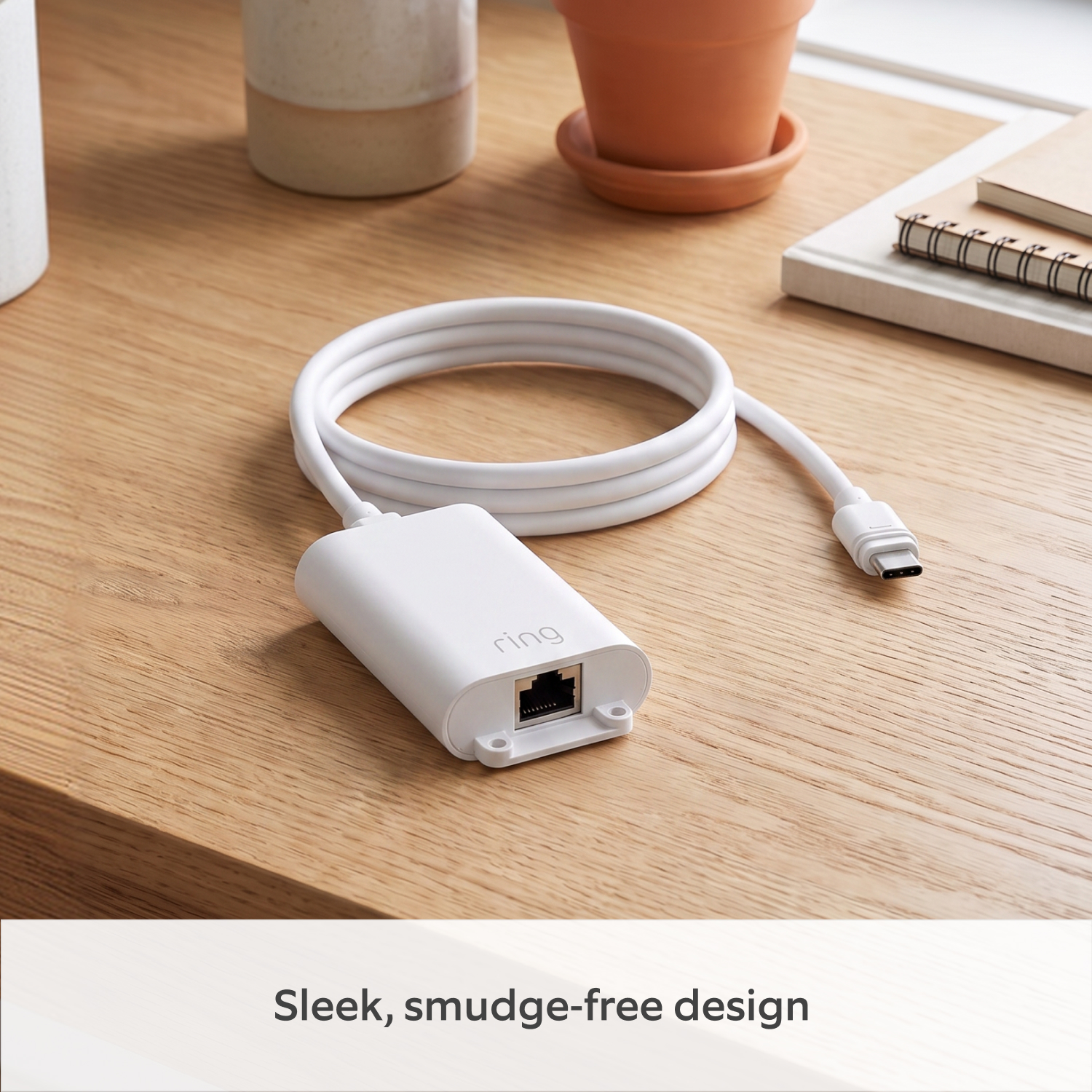 PoE+ to USB-C Indoor Adapter (Indoor Camera 4K and Outdoor Camera 4K Plus) - White PoE+ to USB-C Indoor Adapter with a coiled USB-C cable on a wooden desk, surrounded by ceramic pots and notebooks