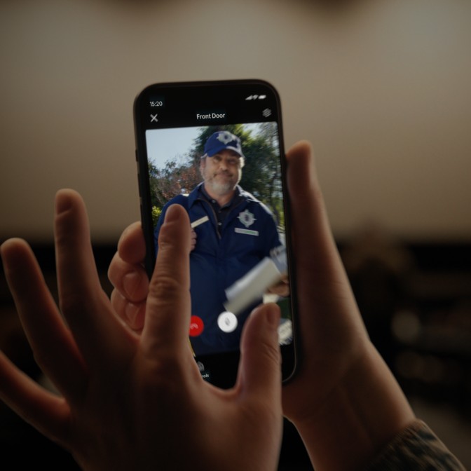 Close-up of someone holding a smartphone displaying footage of a male technician in his blue uniform.