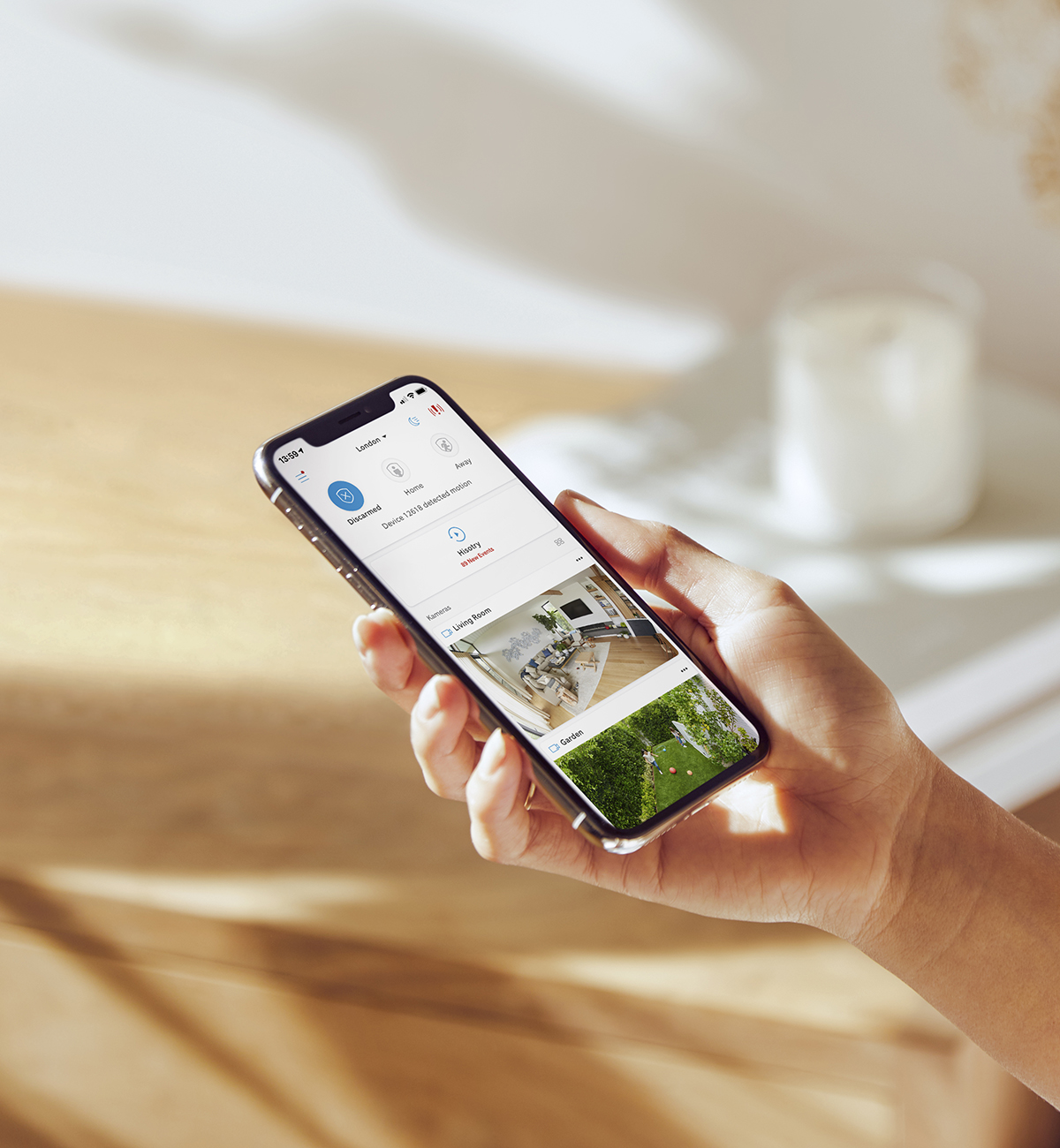 Hand holding phone with Ring app open, showing camera feeds and alarm status for remote home monitoring and control.