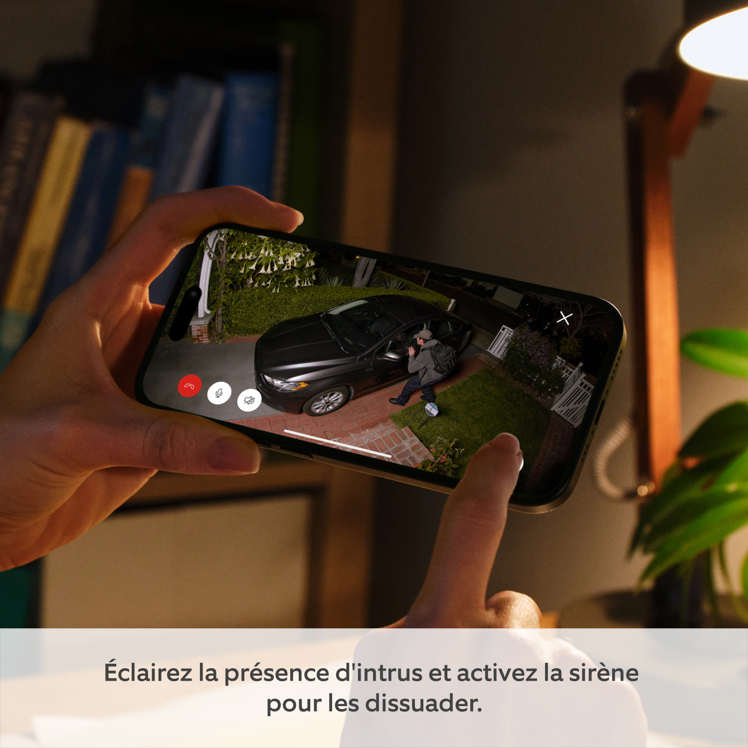 Caméra Spotlight Pro (nouvelle génération) avec adaptateur secteur (for Spotlight Cam Pro Plug-In (2e génération)) - Mains tenant un téléphone montrant l'app Ring avec une personne regardant dans une voiture la nuit, éclairée par Spotlight Cam Pro. Doigt appuie sur sirène